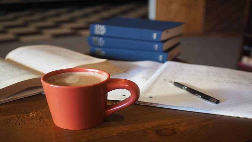 Books, pen, and coffee on desk.
